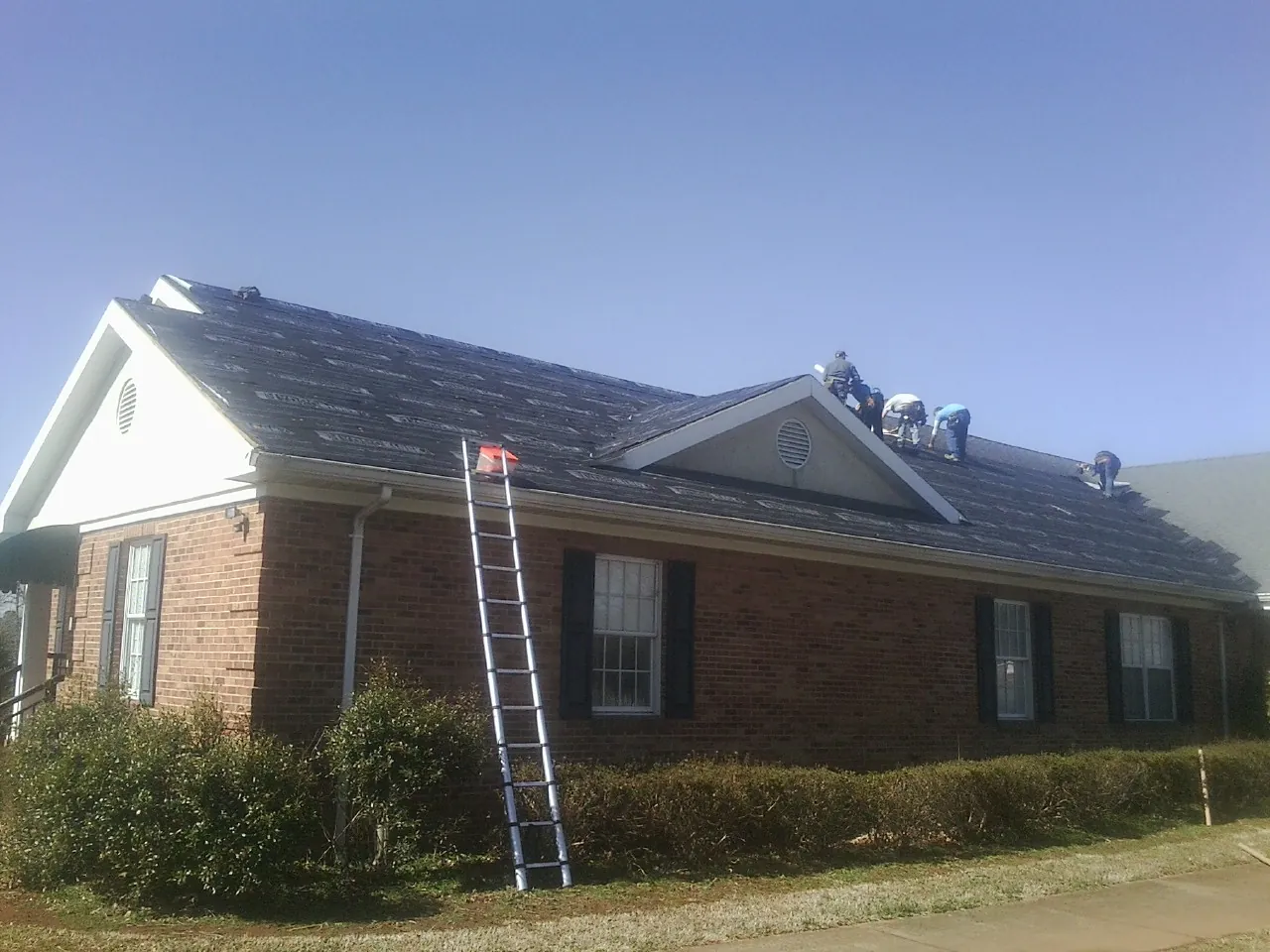 Crew tearing shingles off a brick ranch roof with a ladder set — Metal Roof Repair work by our crew in Attalla