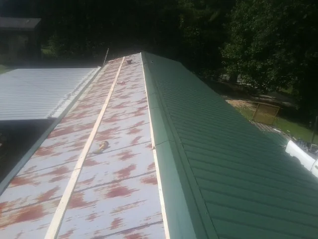 Old rusted panels beside newly installed green metal roofing — Wind Damage Roof Repair by Roofing Brothers in Attalla