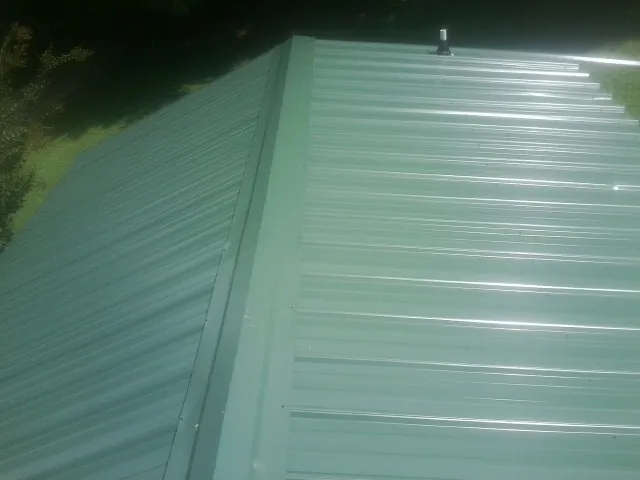 New green metal panels meeting at the ridge of a roof — Flat Roof Repair work by our crew in Attalla