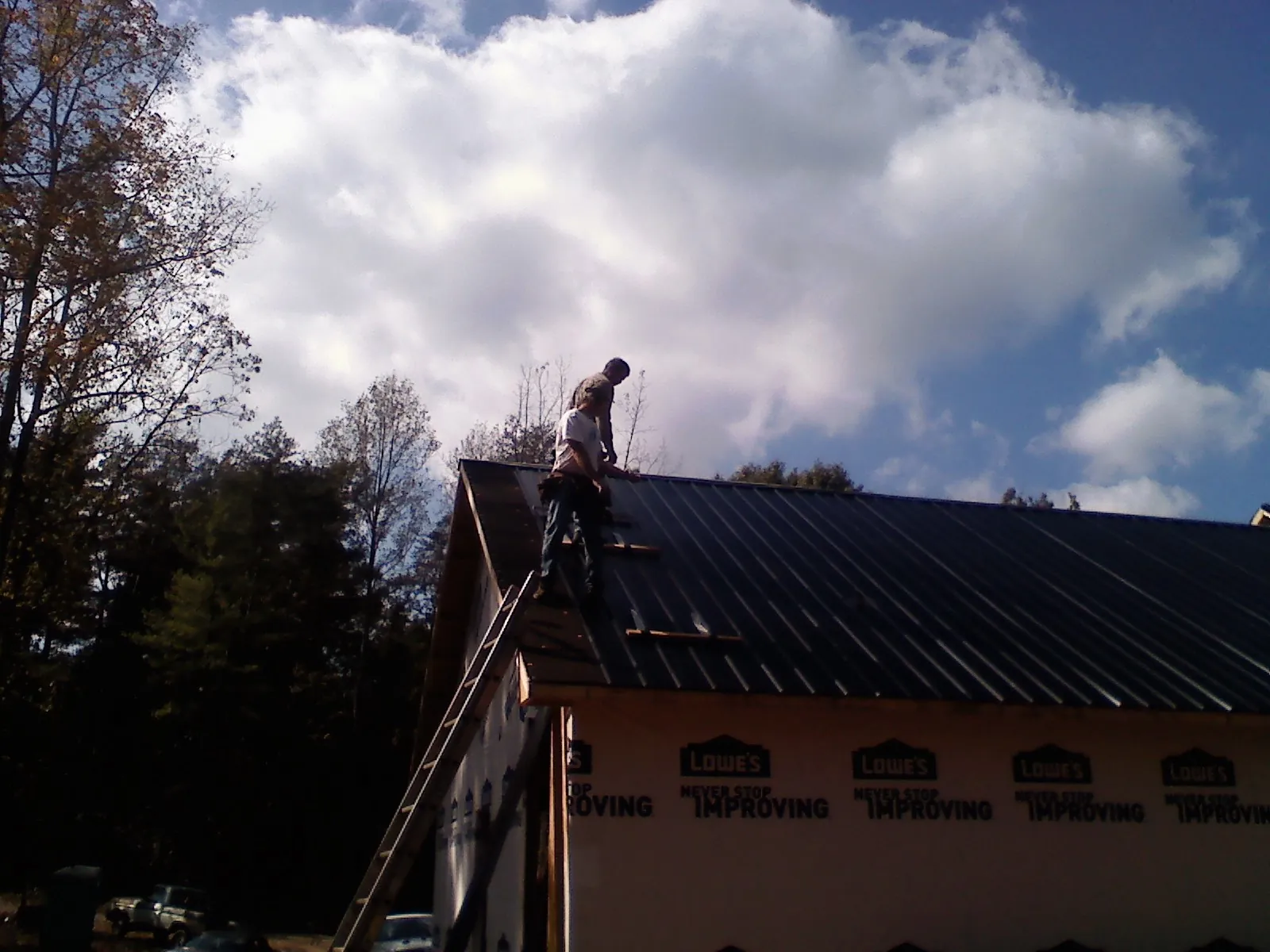 Roofer fastening dark metal panels high against a cloudy sky, from a Roof Inspection job in Attalla