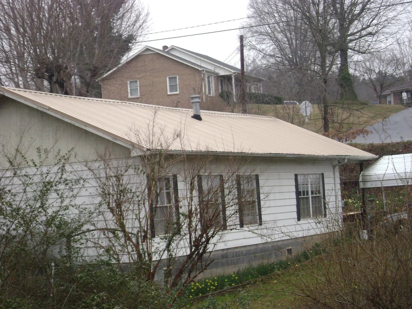 Tan metal roof on a white sided house set into a hillside — Commercial Roofing by Roofing Brothers in Attalla
